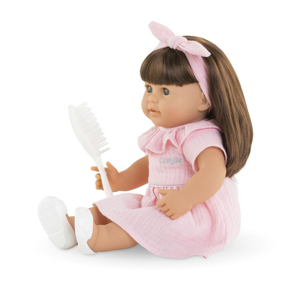 Eine Puppe mit braunen Haaren, die ein rosa Kleid und weiße Schuhe trägt, hält einen Kamm.