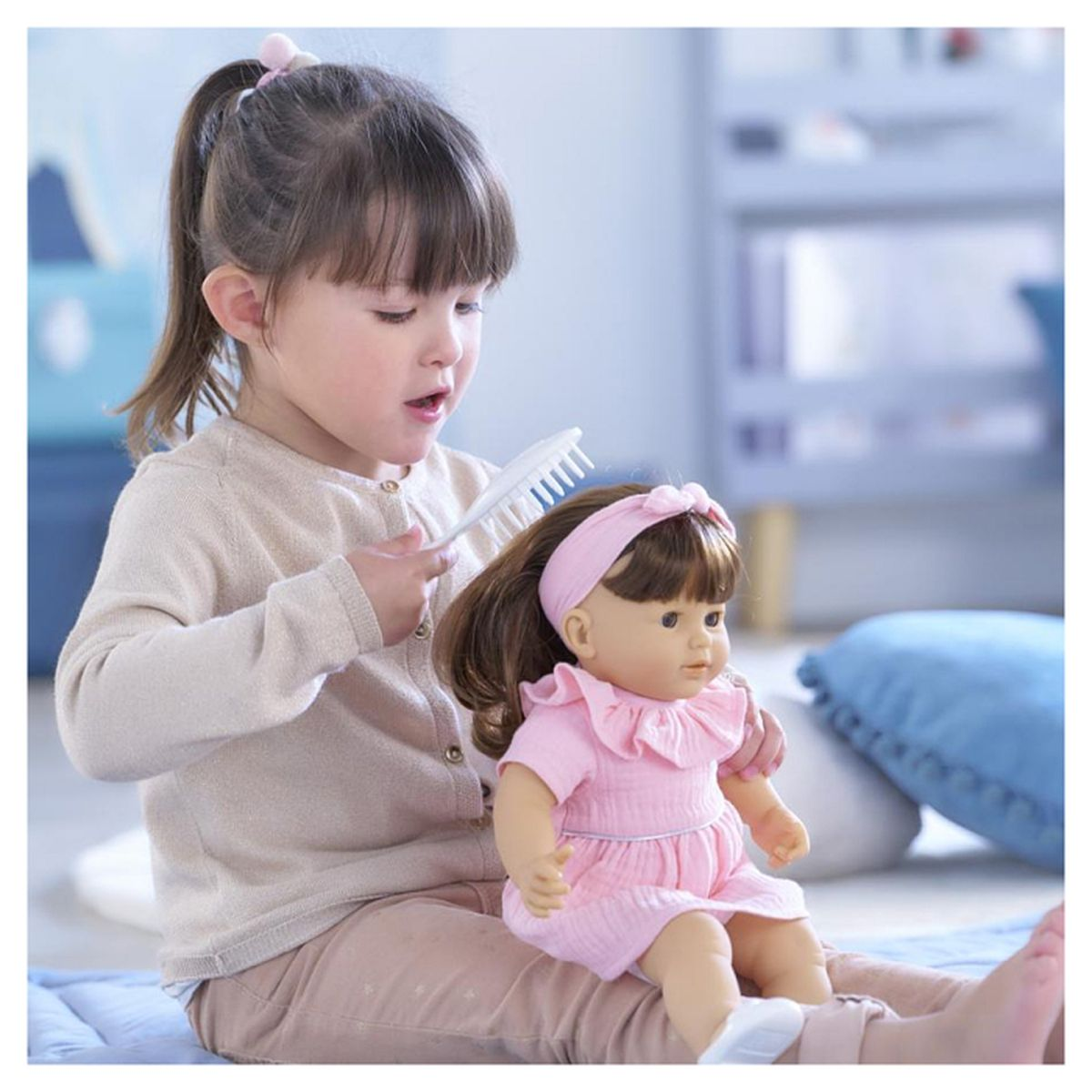 Ein junges Mädchen mit Pferdeschwanz bürstet die Haare einer Puppe. Beide tragen Rosa und Beige.