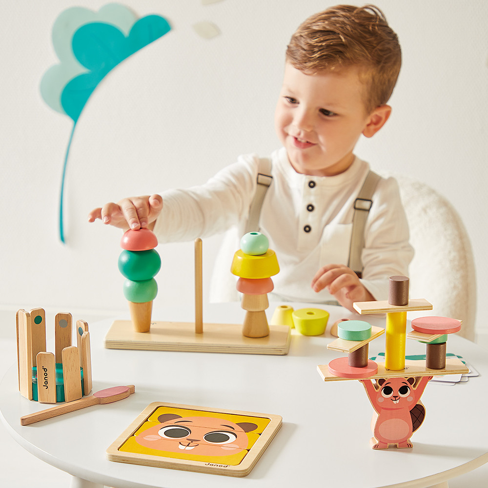 Un jeune garçon joue avec des jouets en bois colorés, dont des tours à empiler de crème glacée et un jeu d'équilibre de castor.