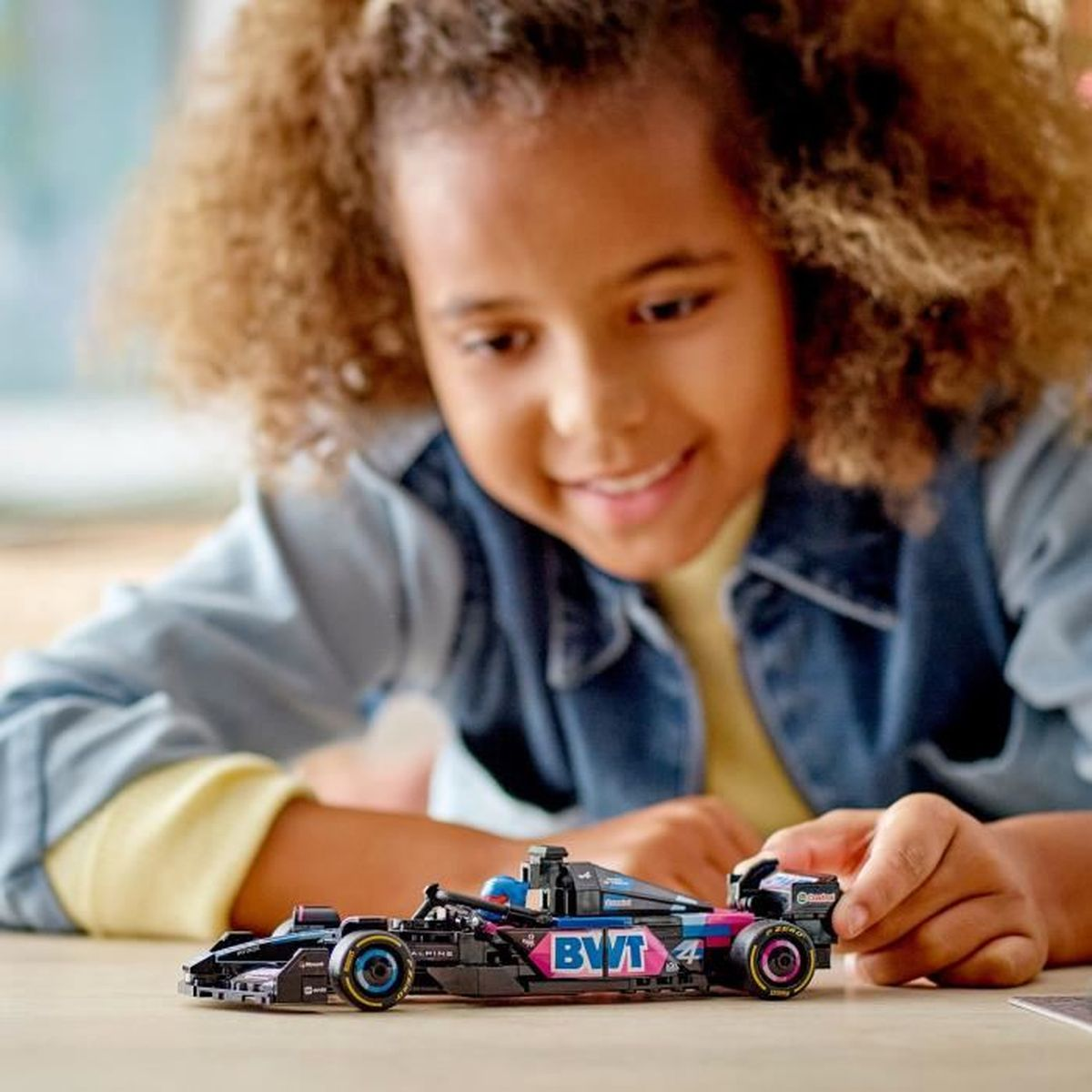 Una bambina con capelli ricci gioca con un'auto giocattolo F1 nera con accenti blu e rosa.