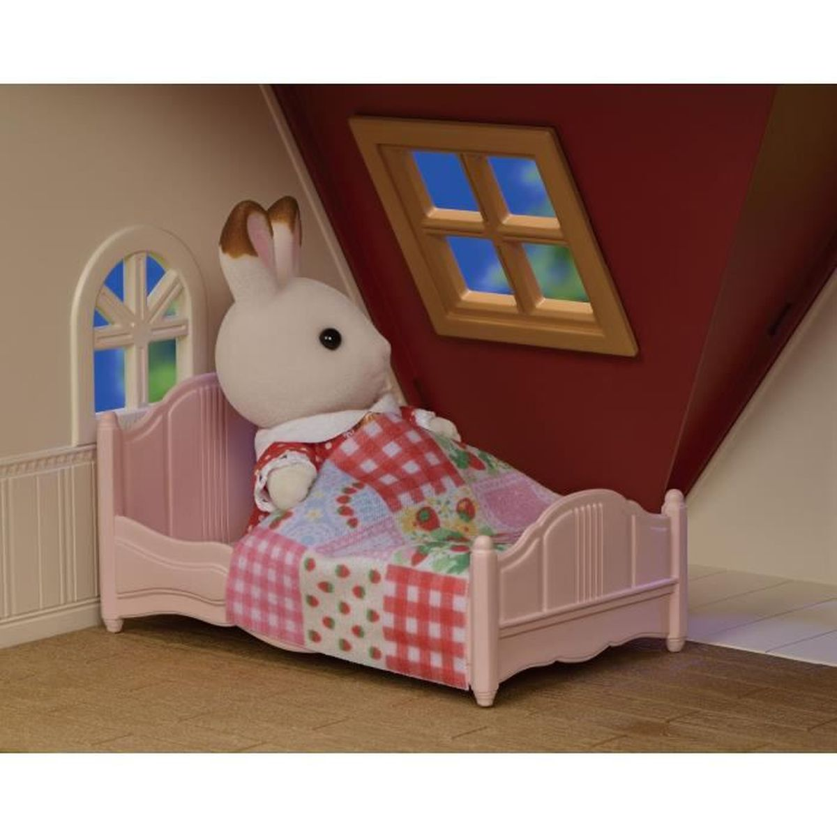 Ein Kaninchen in einem karierten Kleid liegt in einem rosa Bett unter einer bunten Decke.