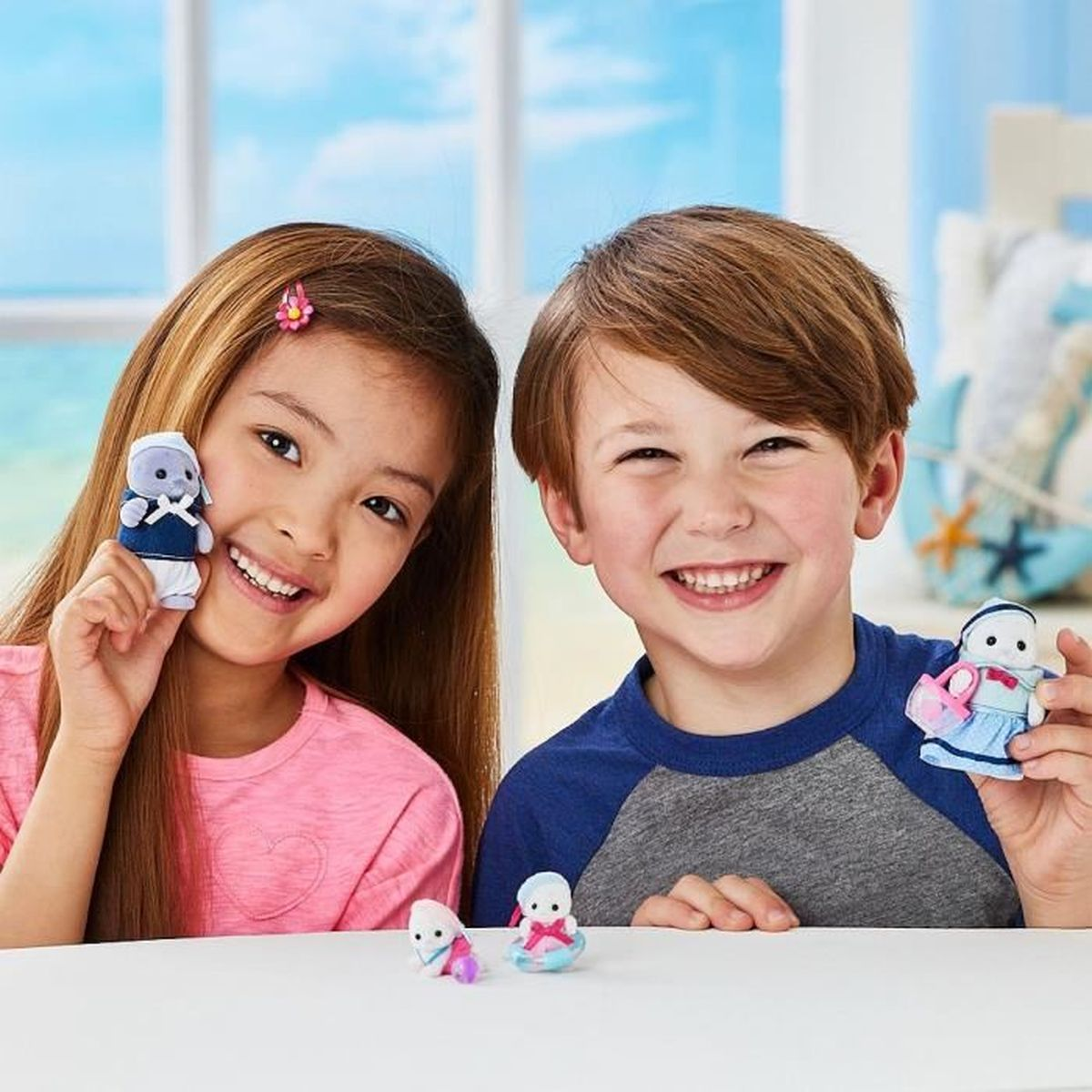 Zwei Kinder halten kleine Spielfiguren. Im Hintergrund ist ein Meerblick.