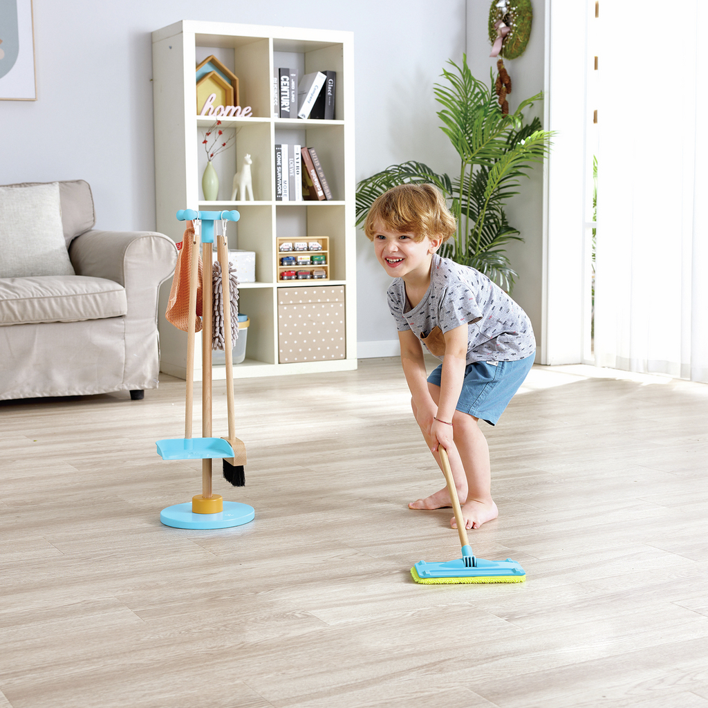 Un niño juega con un set de limpieza de juguete cerca de una estantería y un sofá.