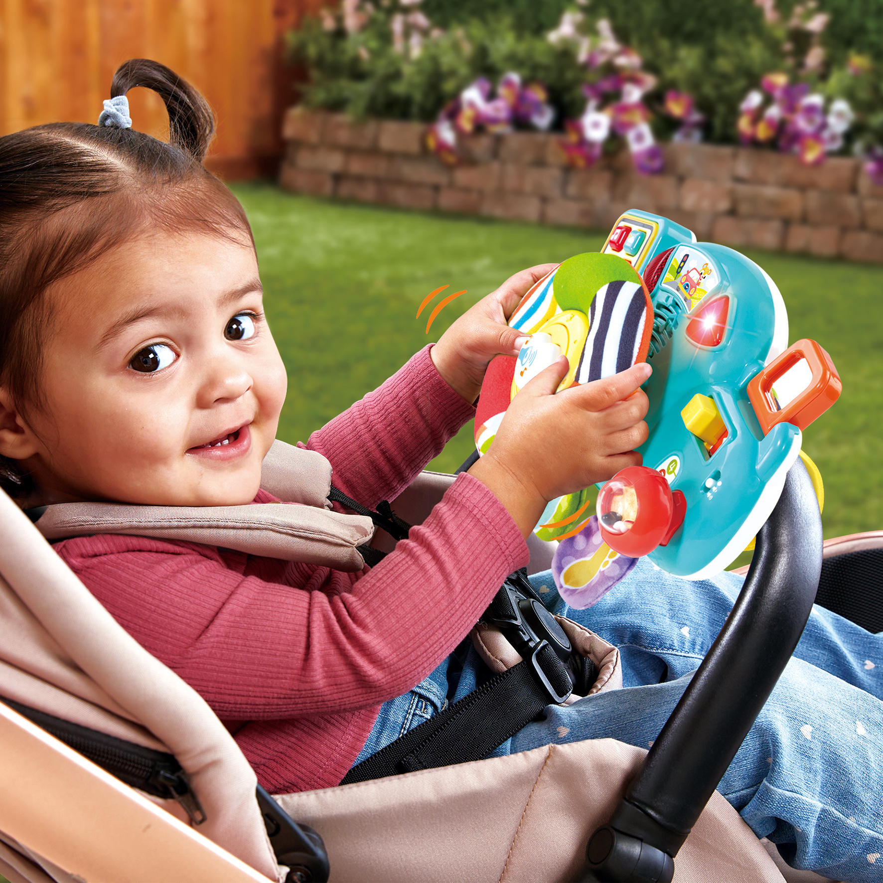 Una bambina seduta in un passeggino gioca felicemente con un volante giocattolo.