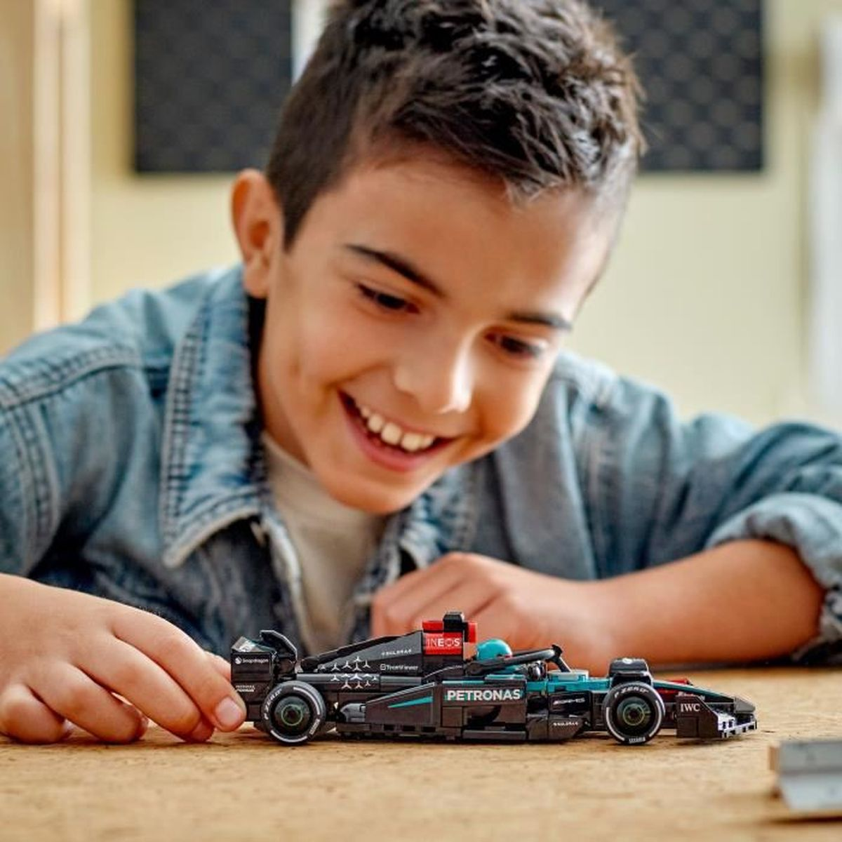 Mavi kot gömlekli bir çocuk siyah bir F1 Lego araba yapıyor.