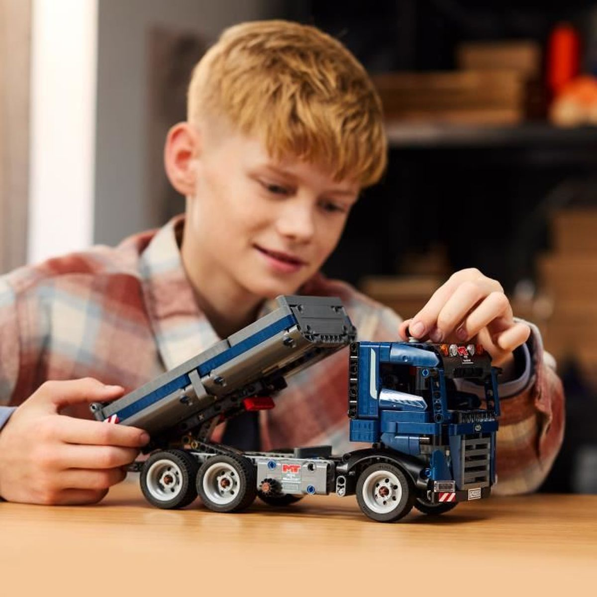 Bir oğlan mavi Lego kamyon yapıyor. Damperli römork kaldırılmış durumda.