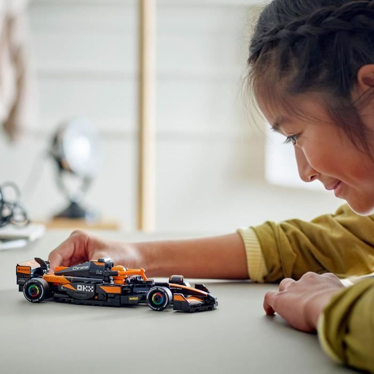 Bir kız, turuncu ve siyah Lego Formula 1 arabasına bakıyor.