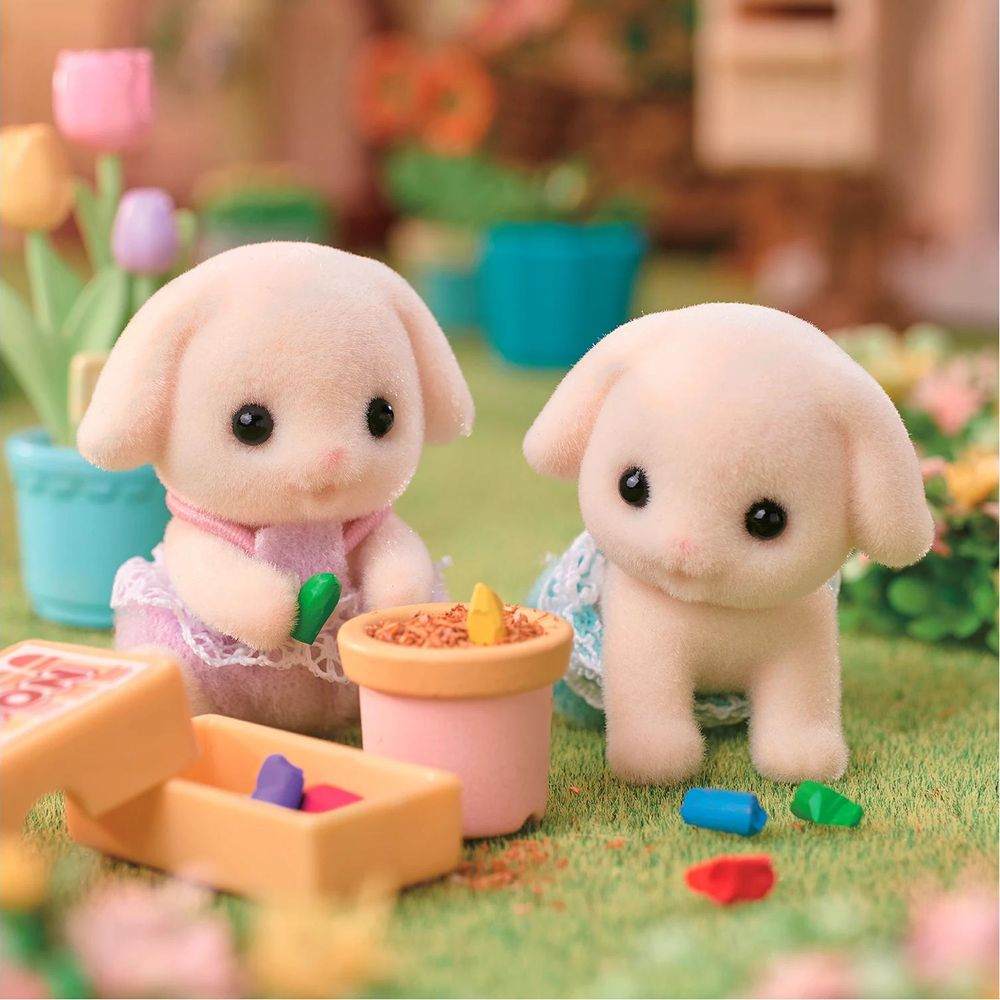 Dos conejitos de peluche en un jardín con herramientas de jardinería de juguete y una planta.