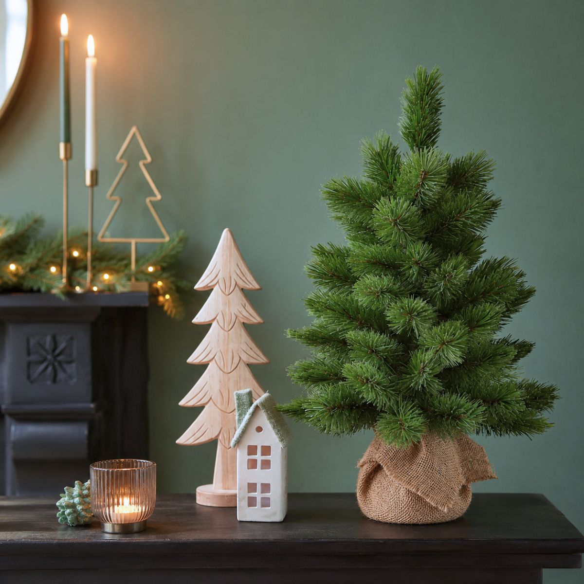 Un petit sapin de Noël sur une table avec des bougies, des arbres en bois et une maison.