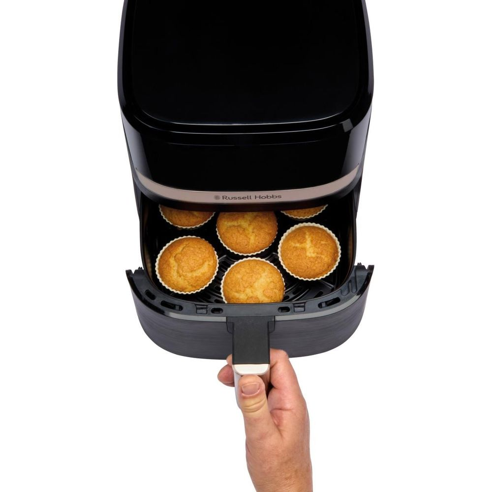 Una mano estrae un cestello con sei muffin da una friggitrice ad aria nera.