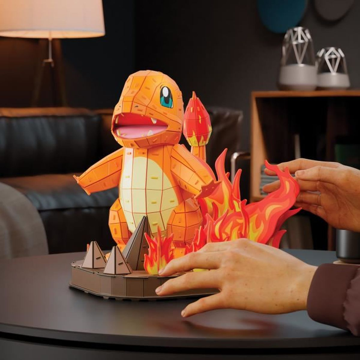 Figura naranja de Charmander con llamas sobre una mesa, manos visibles.