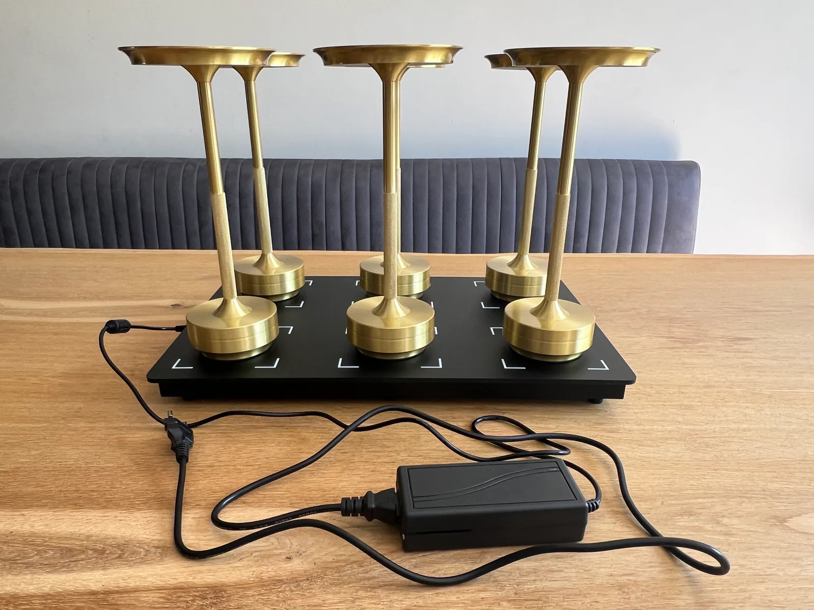 Sechs goldene Kerzenhalter auf einer schwarzen Basis mit Kabeln und Netzteil.