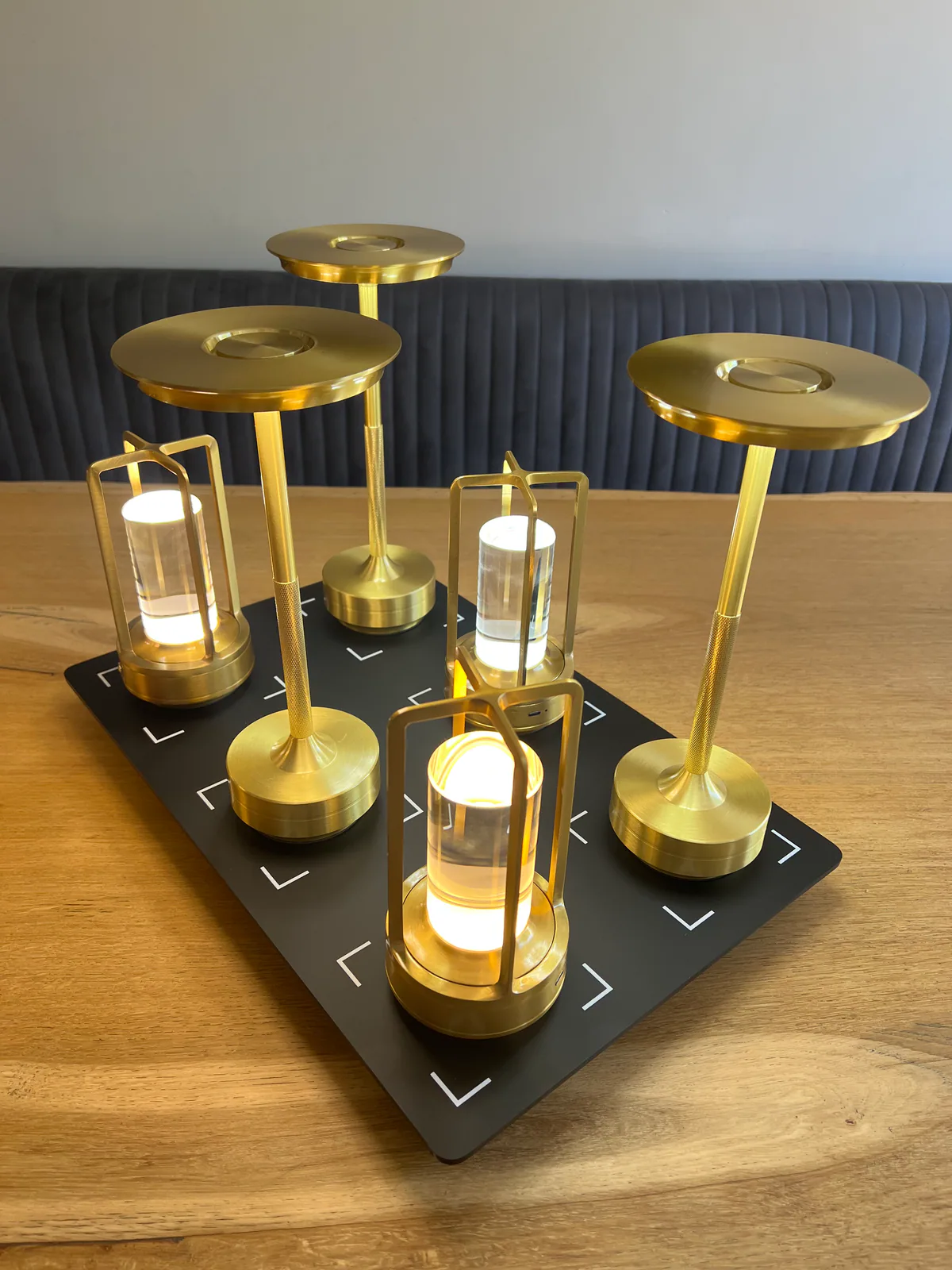 Fünf goldene Tischlampen mit zylindrischen Glaskörpern auf schwarzer Unterlage.