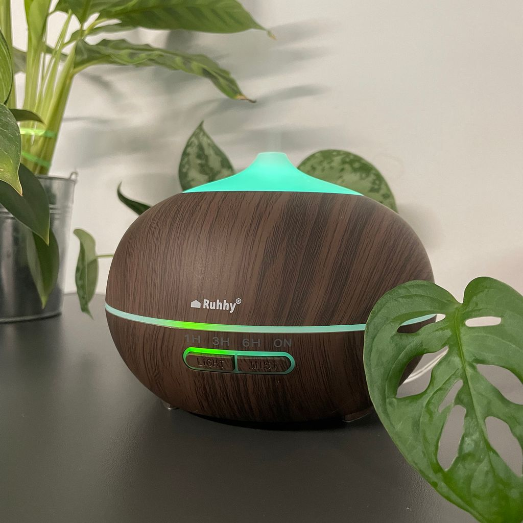 Ein dunkler Holz-Diffusor mit grünem Licht leuchtet neben Pflanzen.
