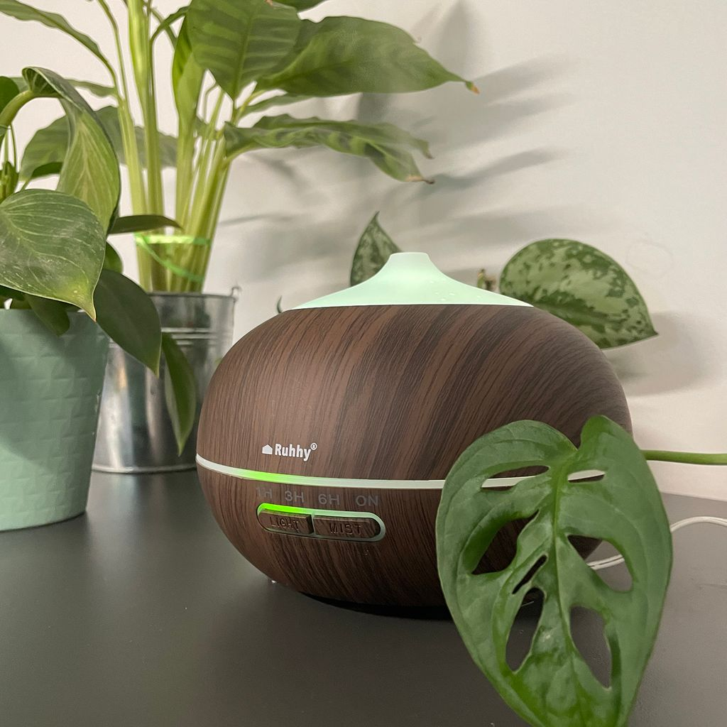 Ein brauner Diffusor mit Holzmaserung steht neben grünen Pflanzen.