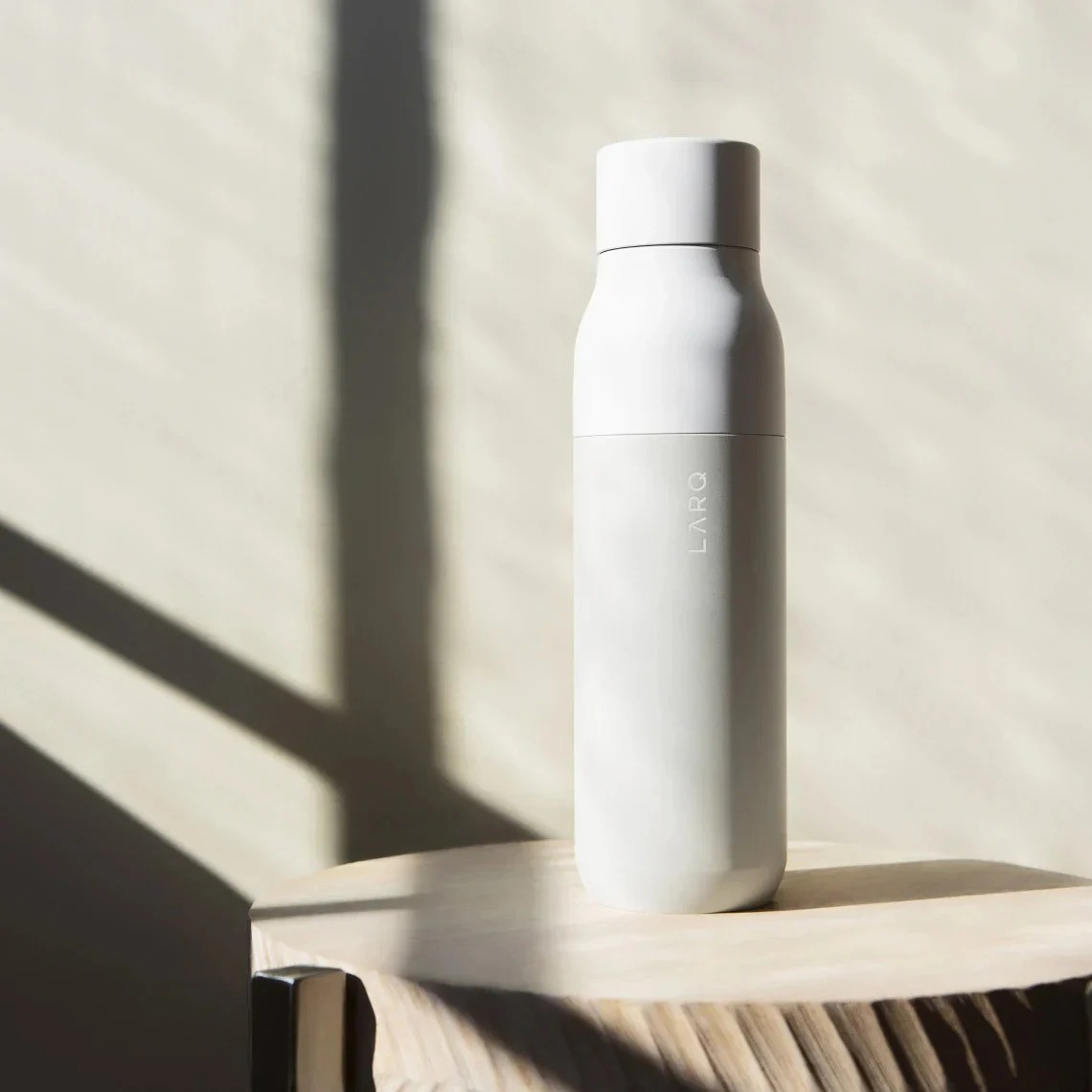 Eine weiße LARQ-Flasche steht im Schatten auf einem Holztisch.