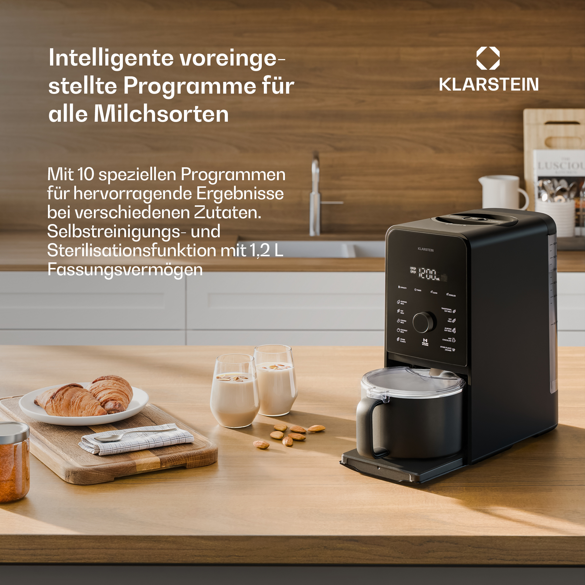 Ein schwarzer Klarstein Milchzubereiter steht auf einem Holztisch mit Croissants und Nüssen.