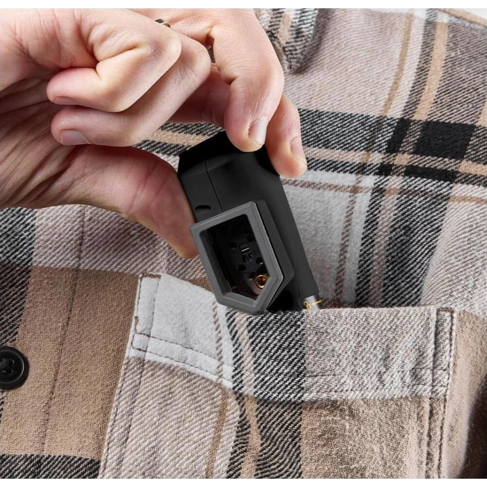 Eine Hand steckt ein schwarzes Gerät mit grauem Adapter in eine karierte Hemdtasche.
