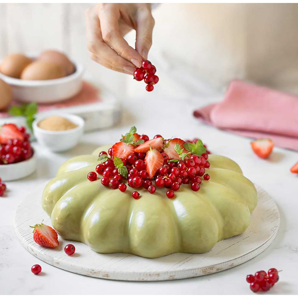 Eine Hand garniert einen grünen Kuchen mit roten Johannisbeeren und Erdbeeren.