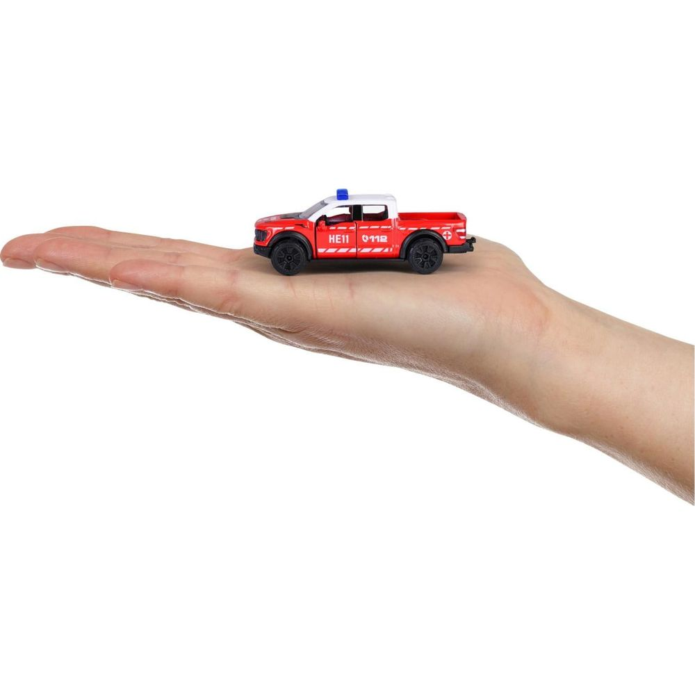 Ein rotes Spielzeug-Feuerwehrauto mit weißem Dach und blauer Sirene auf einer Hand.