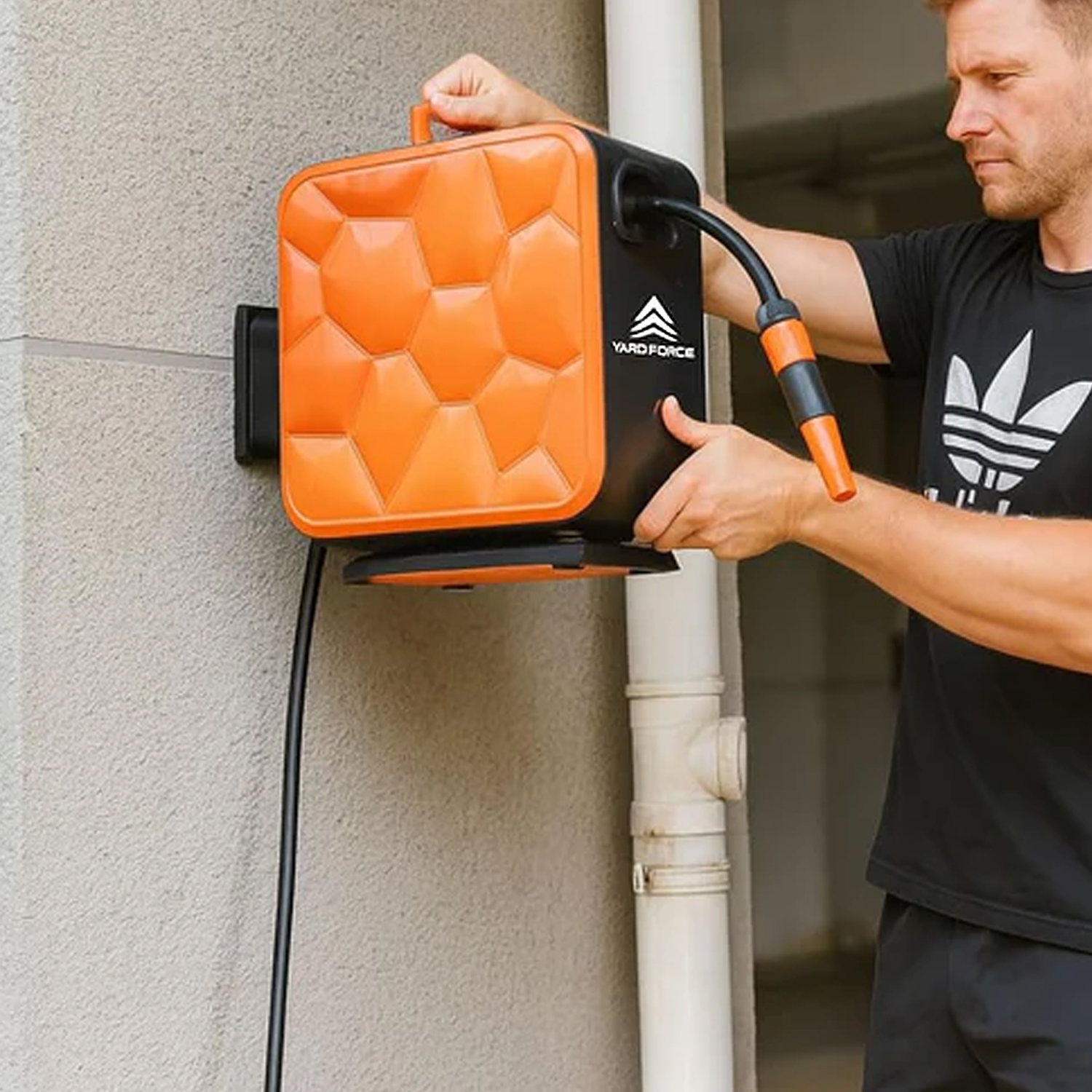Mann montiert eine orange und schwarze Schlauchaufwicklung an einer Wand neben einem Rohr.