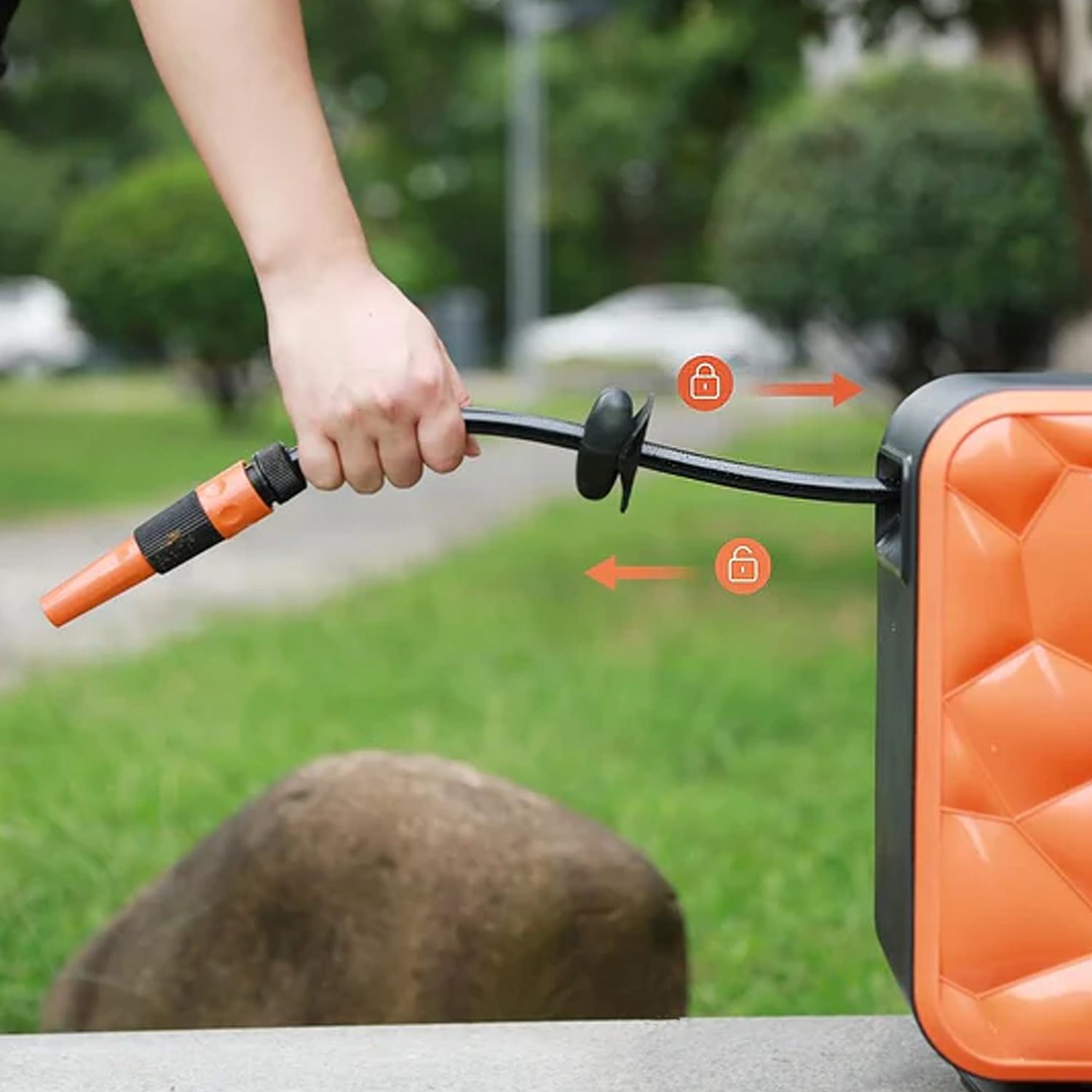 Hand hält orange Schlauchdüse, nahe schwarzem Schlauch auf orange Rolle.