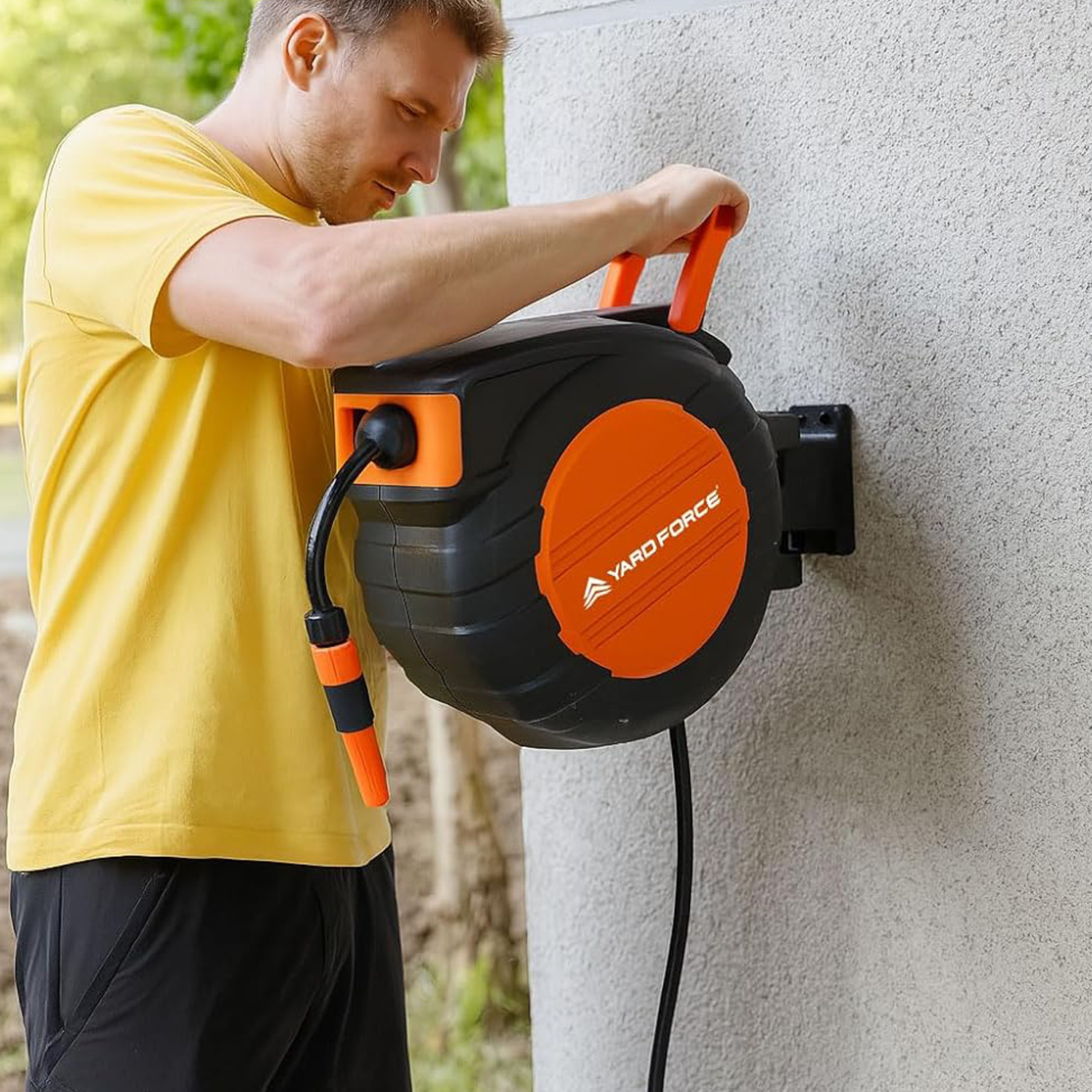 Mann in gelbem T-Shirt befestigt einen schwarzen und orangen Schlauchaufroller an einer Wand.