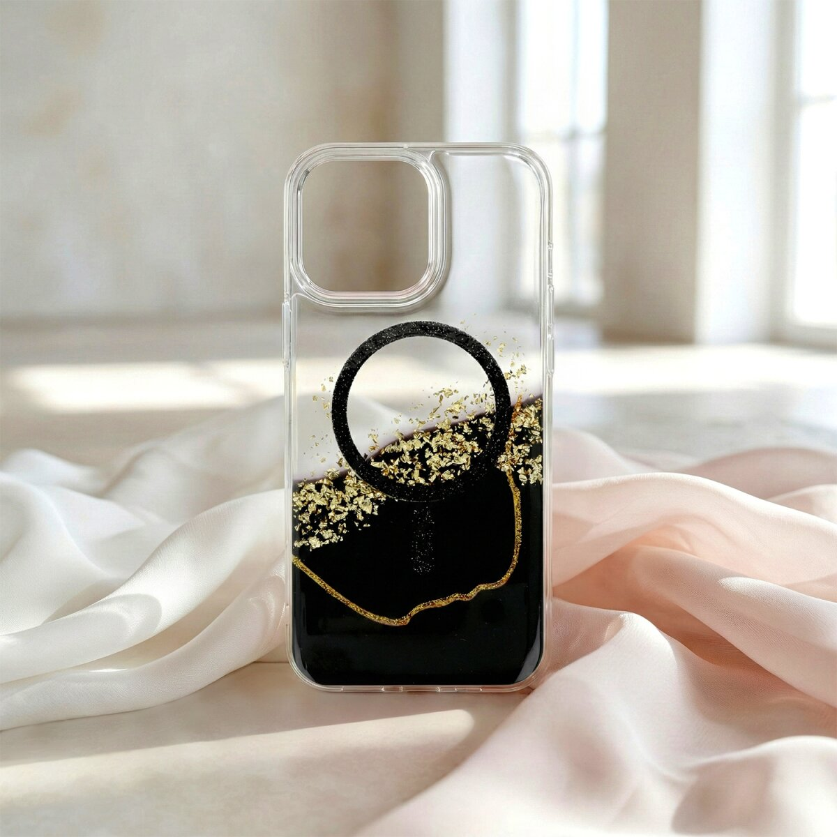 Transparente Hülle mit schwarzem und goldfarbenem Design, auf Stoff drapiert.