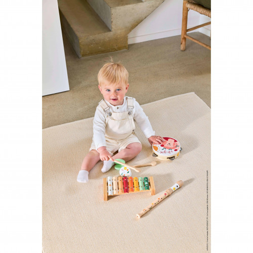 Ein Baby sitzt auf einem Teppich mit Spielzeuginstrumenten wie einem Xylophon und einer Trommel.