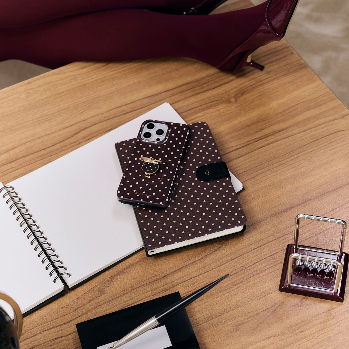 Ein Handy mit Polka-Dot-Hülle und Ringhalter liegt neben einem Notizbuch.