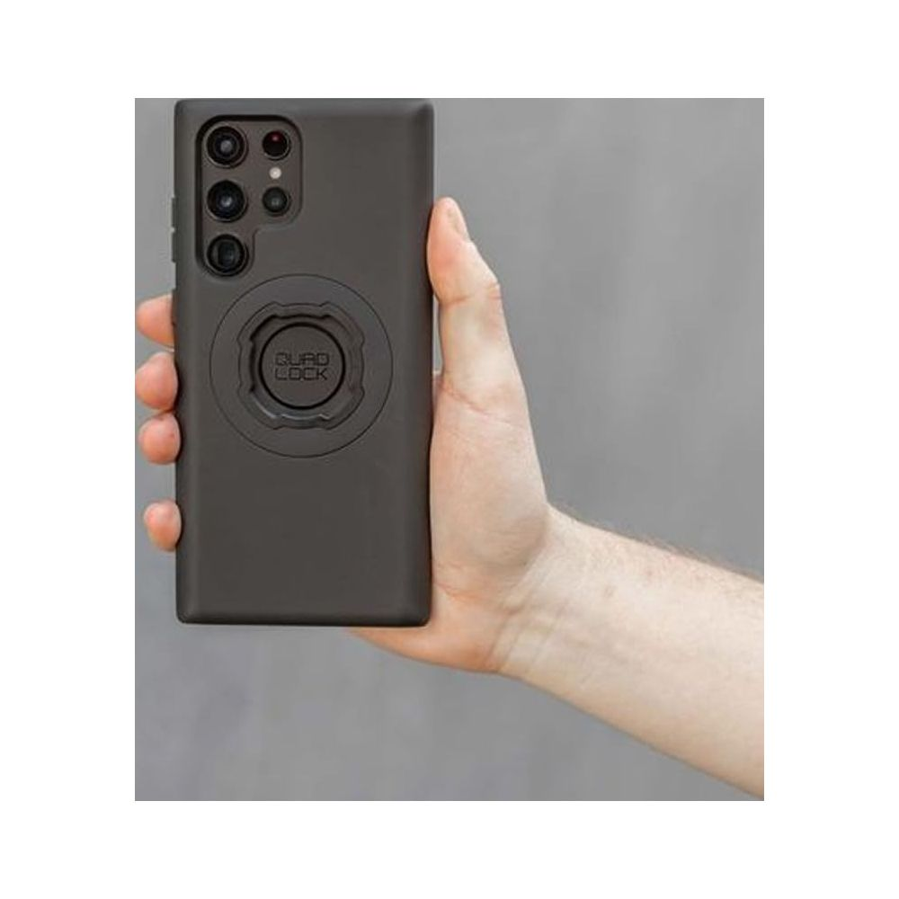 Una mano tiene una custodia per telefono grigio scuro con supporto Quad Lock.