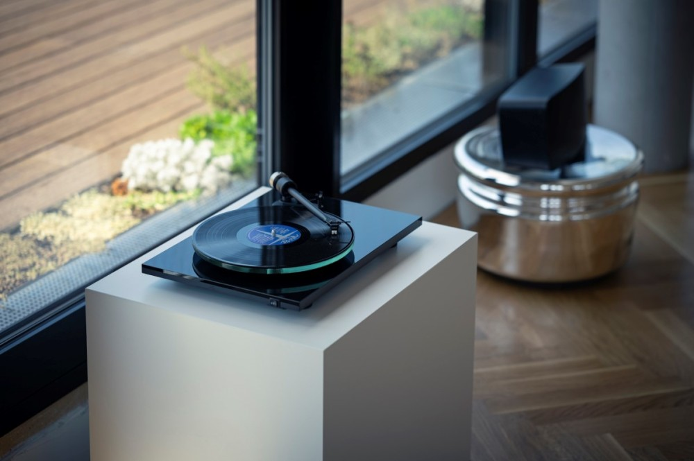 Gramofon z płytą winylową na białym postumencie obok okna.