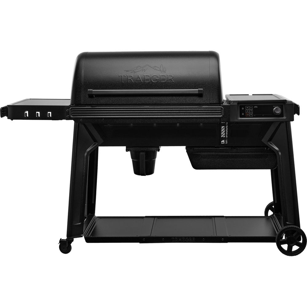 Un gril à granulés Traeger noir avec tablette latérale et commandes numériques repose sur un support à roulettes.