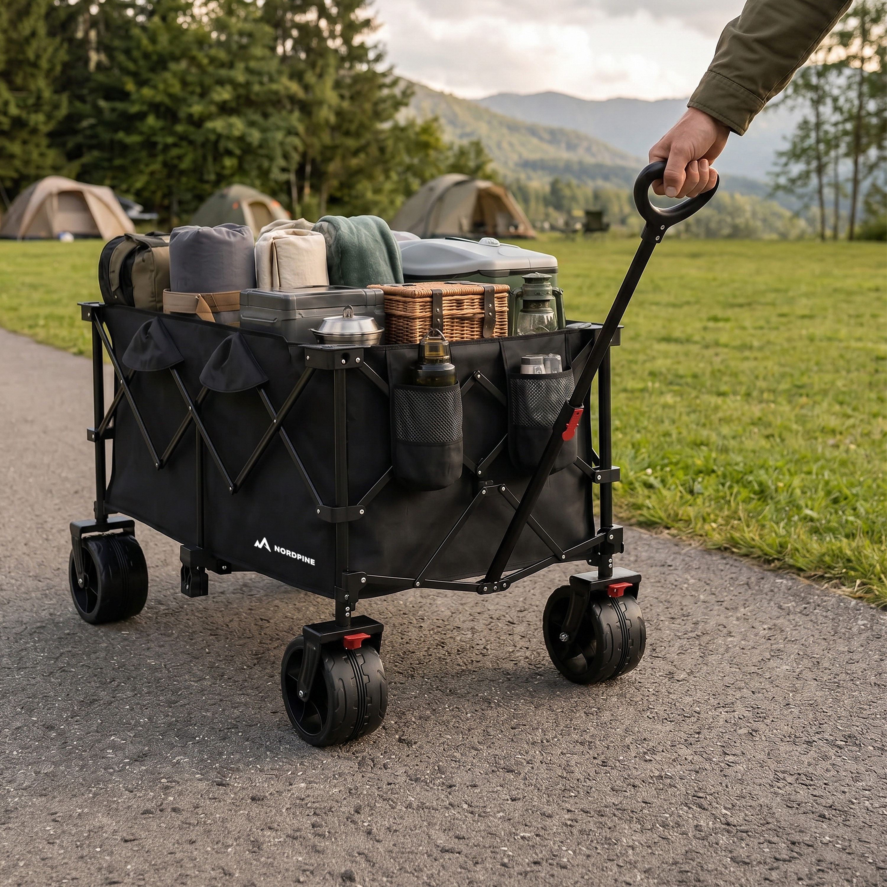 Ein Mann schiebt einen voll beladenen Campingwagen im Freien, Berge im Hintergrund.