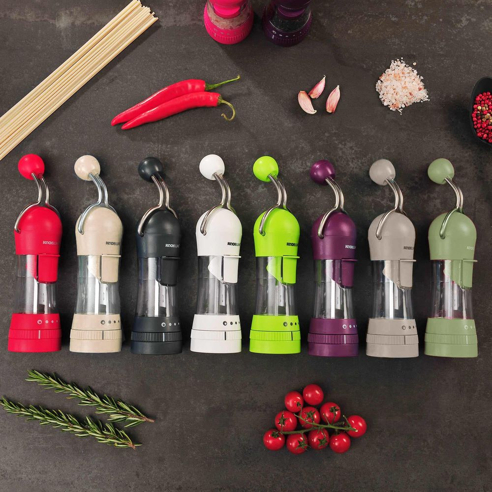 A row of colorful spice grinders with pasta, chili, garlic, salt, and tomatoes.