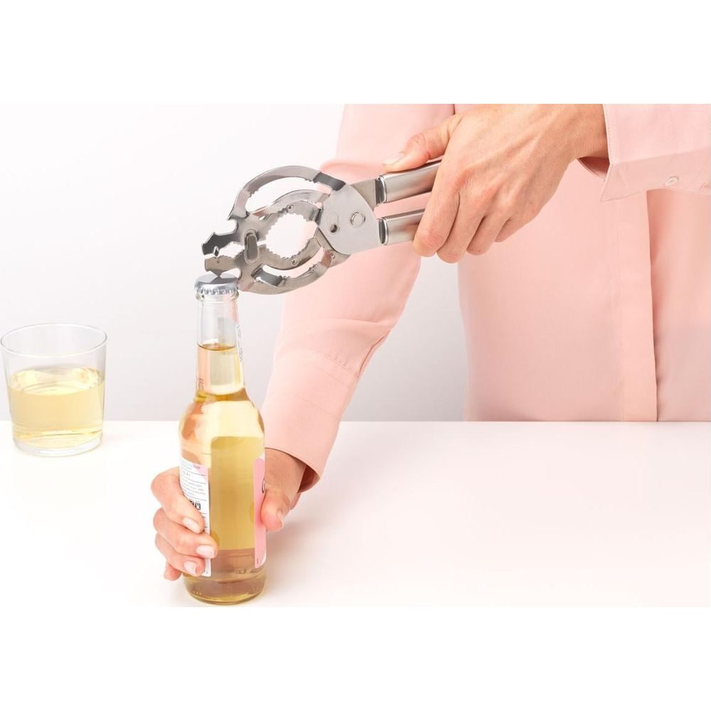 Eine Person öffnet eine Flasche mit einem Mehrzwecköffner neben einem Glas Getränk.