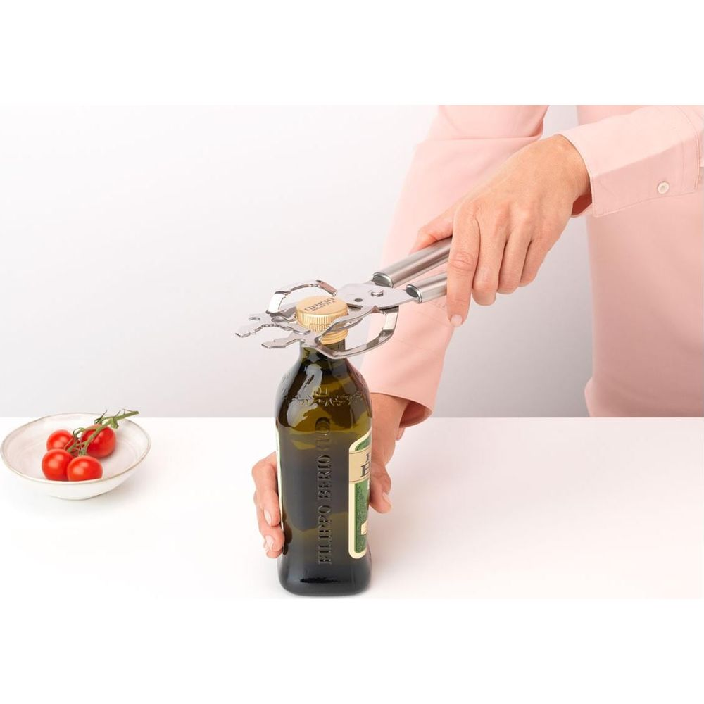 Eine Person benutzt einen silbernen Flaschenöffner, um eine Kappe von einer grünen Olivenölflasche zu schrauben.
