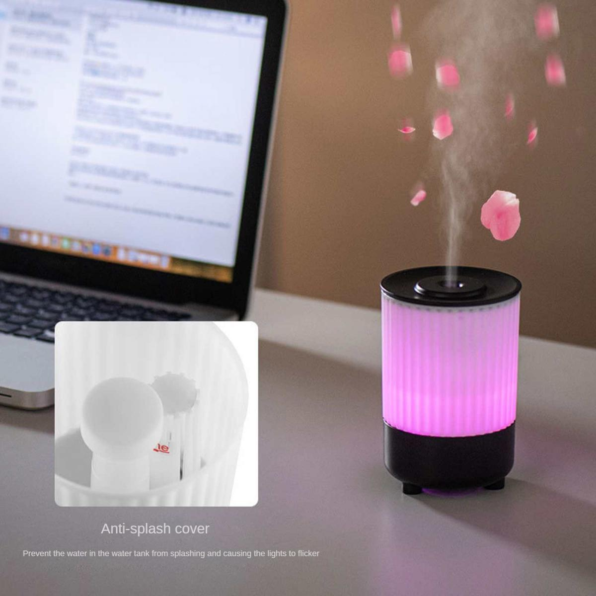 Ein Diffusor mit pinker Beleuchtung und Blütenblättern, neben einem Laptop.