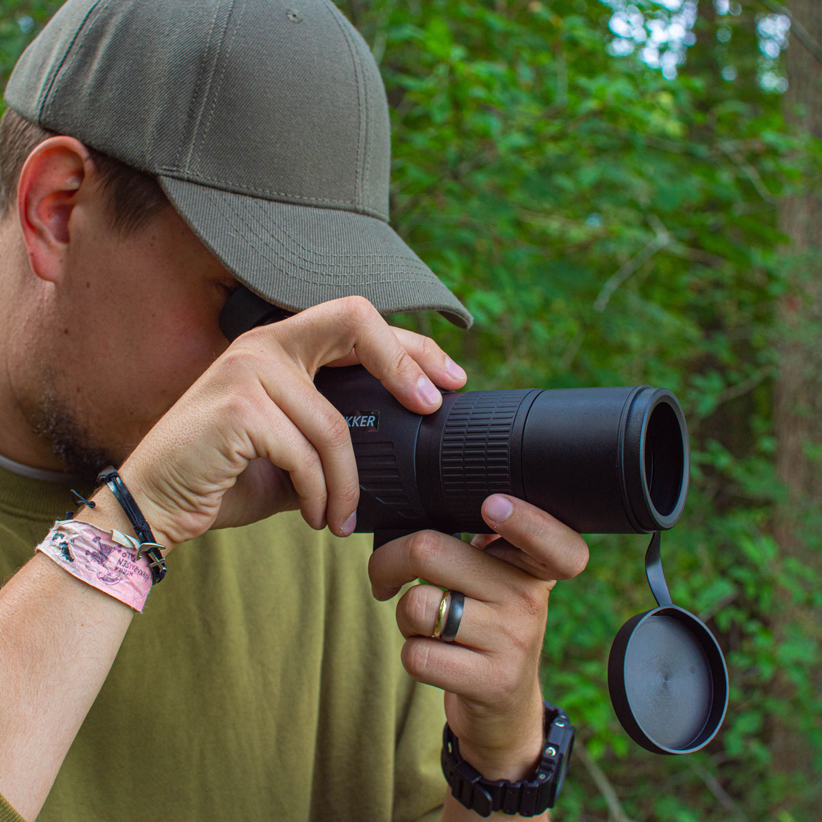 Mann mit grünem Hut blickt durch ein schwarzes Fernglas im Wald.