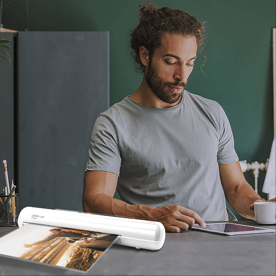 Mann laminiert ein Foto. Er hält eine Tasse Kaffee und benutzt ein Tablet.