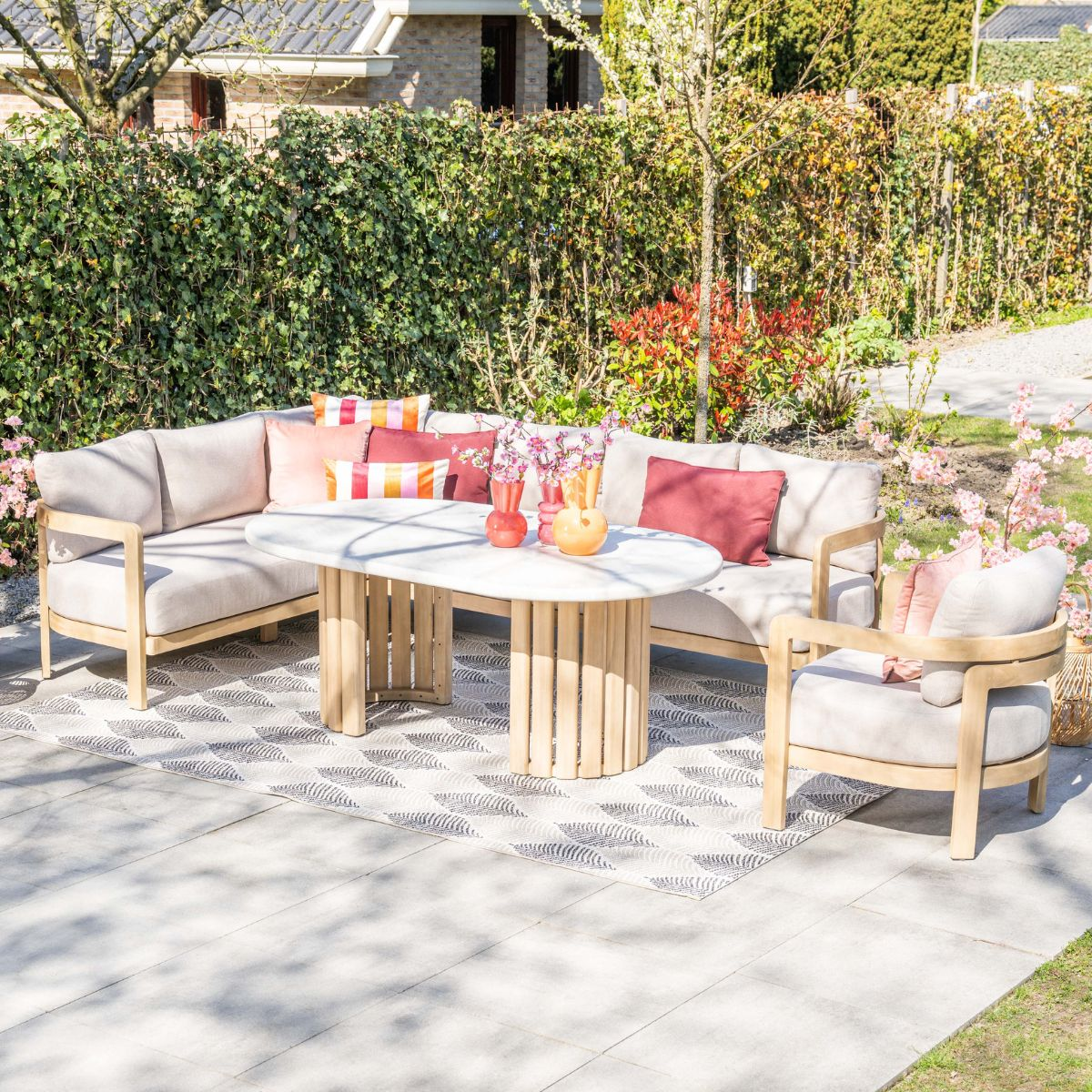 Buitenbank en stoel met ovale tafel op een patio. Groene heg achtergrond.