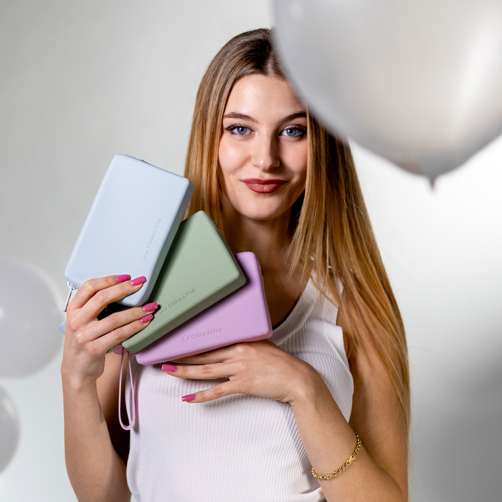 Una donna tiene tre custodie colorate. Palloncini bianchi sullo sfondo.