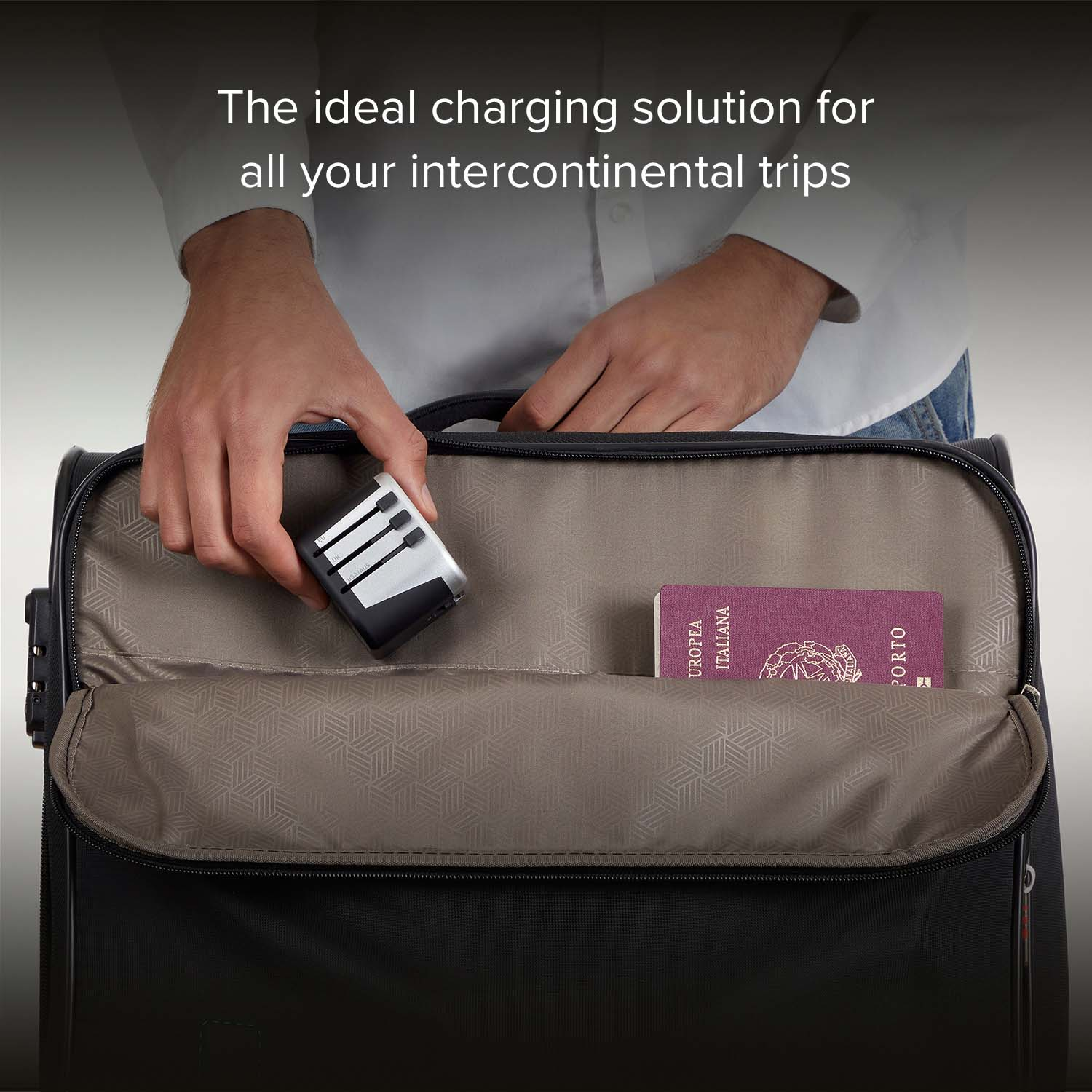 Una mano coloca un adaptador de viaje en una bolsa negra abierta. Se ve un pasaporte italiano.