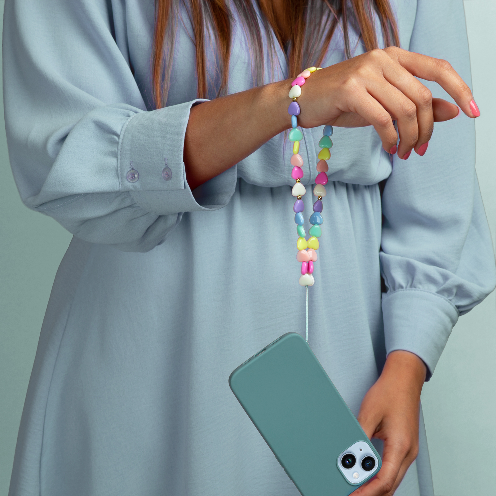 Una donna in abito blu tiene un telefono con un laccetto portachiavi a cuore colorato.