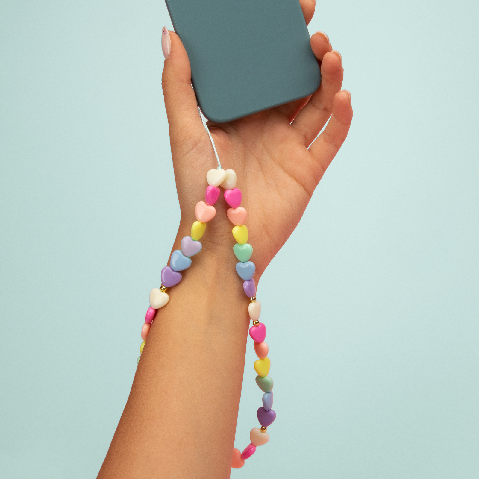 Una mano tiene un telefono con un cinturino di perline a forma di cuore colorate.