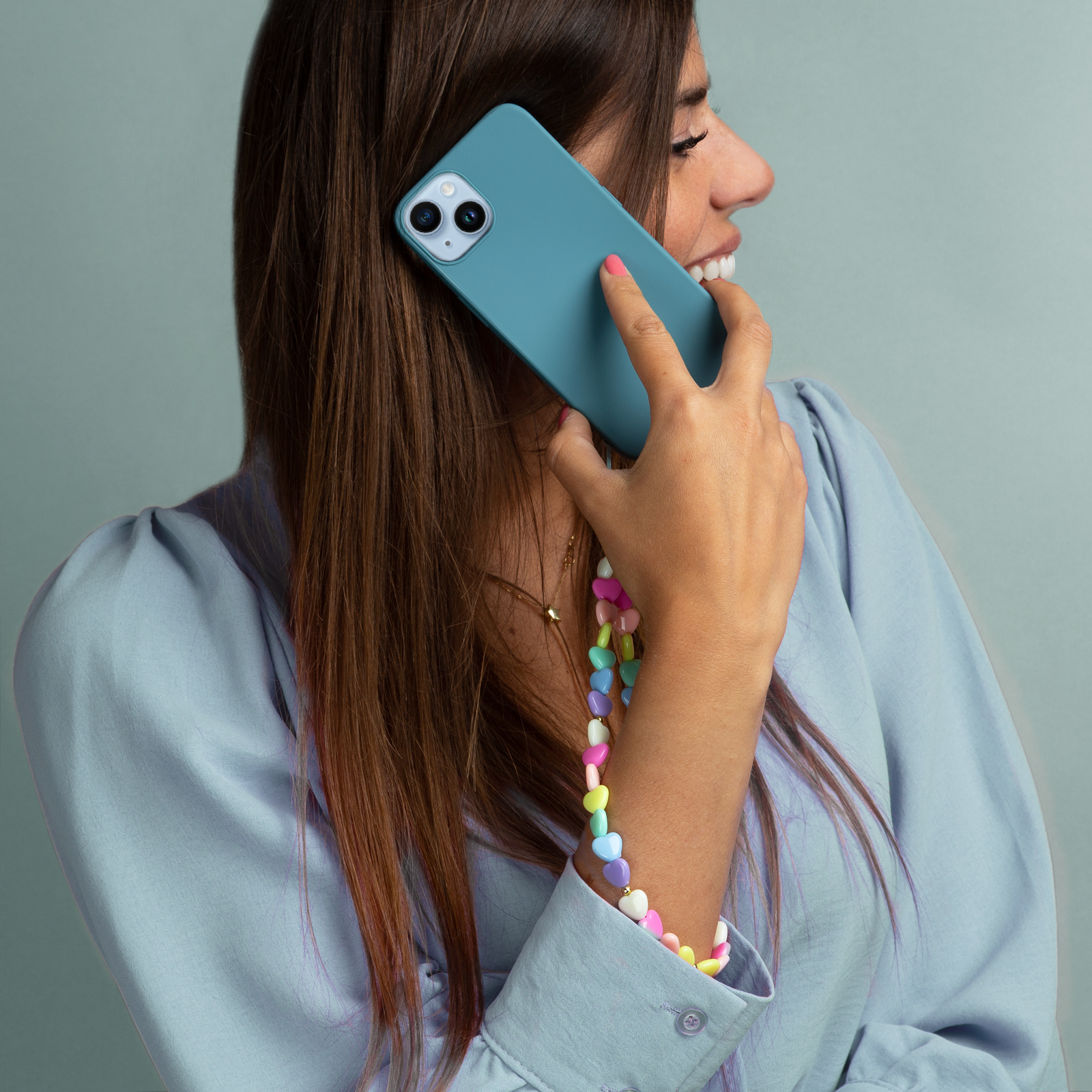 Una donna al telefono con un telefono blu adornato da una collana di perline a forma di cuore.
