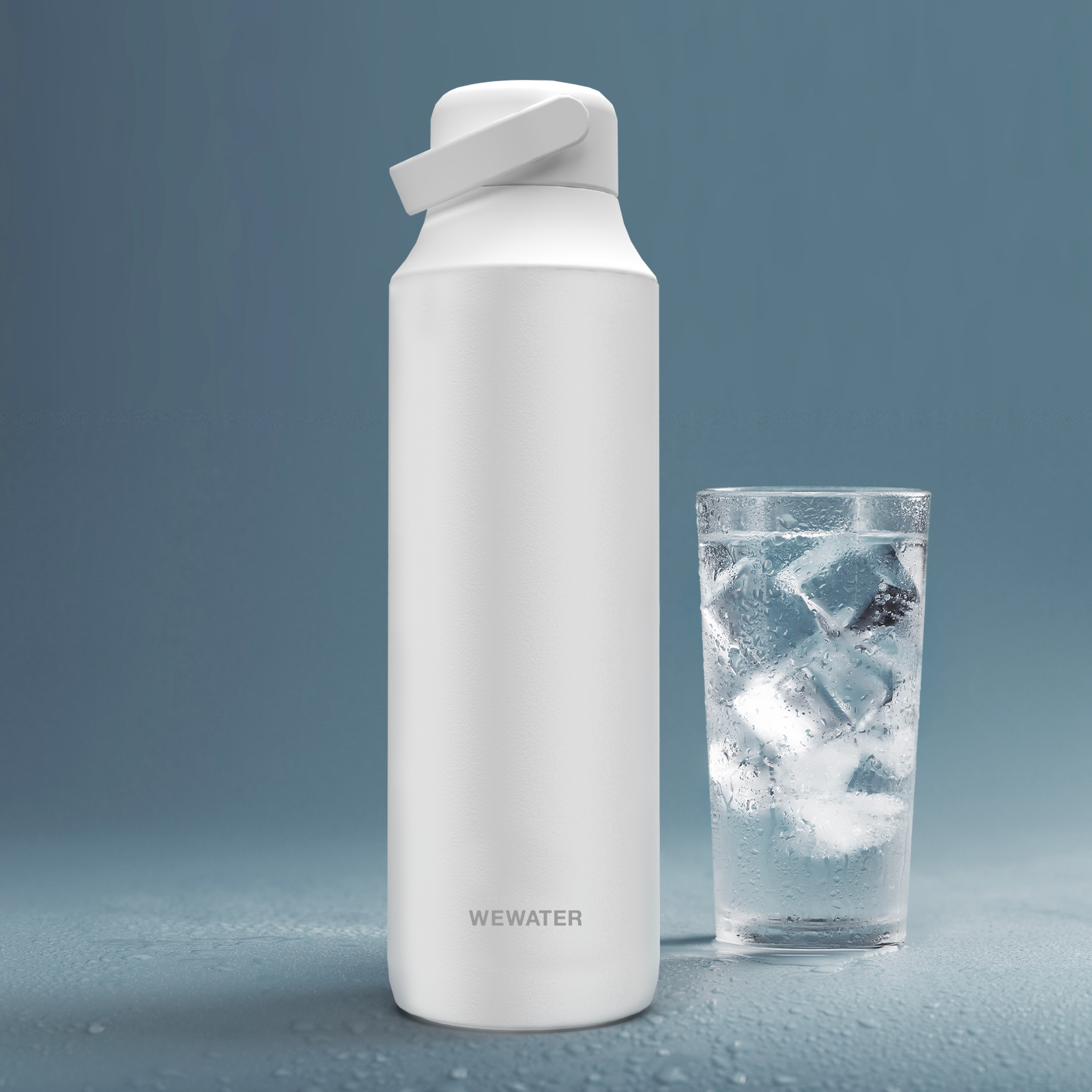 Botella de agua blanca junto a un vaso de agua con cubitos de hielo sobre fondo azul.