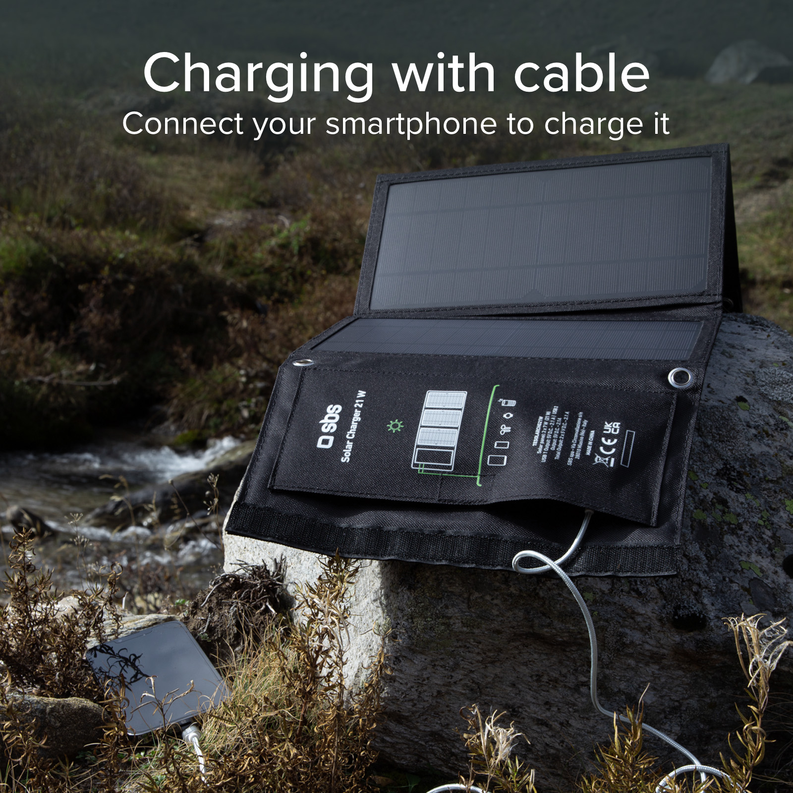 Un caricabatterie solare con cavo sta caricando uno smartphone in un ambiente naturale roccioso.