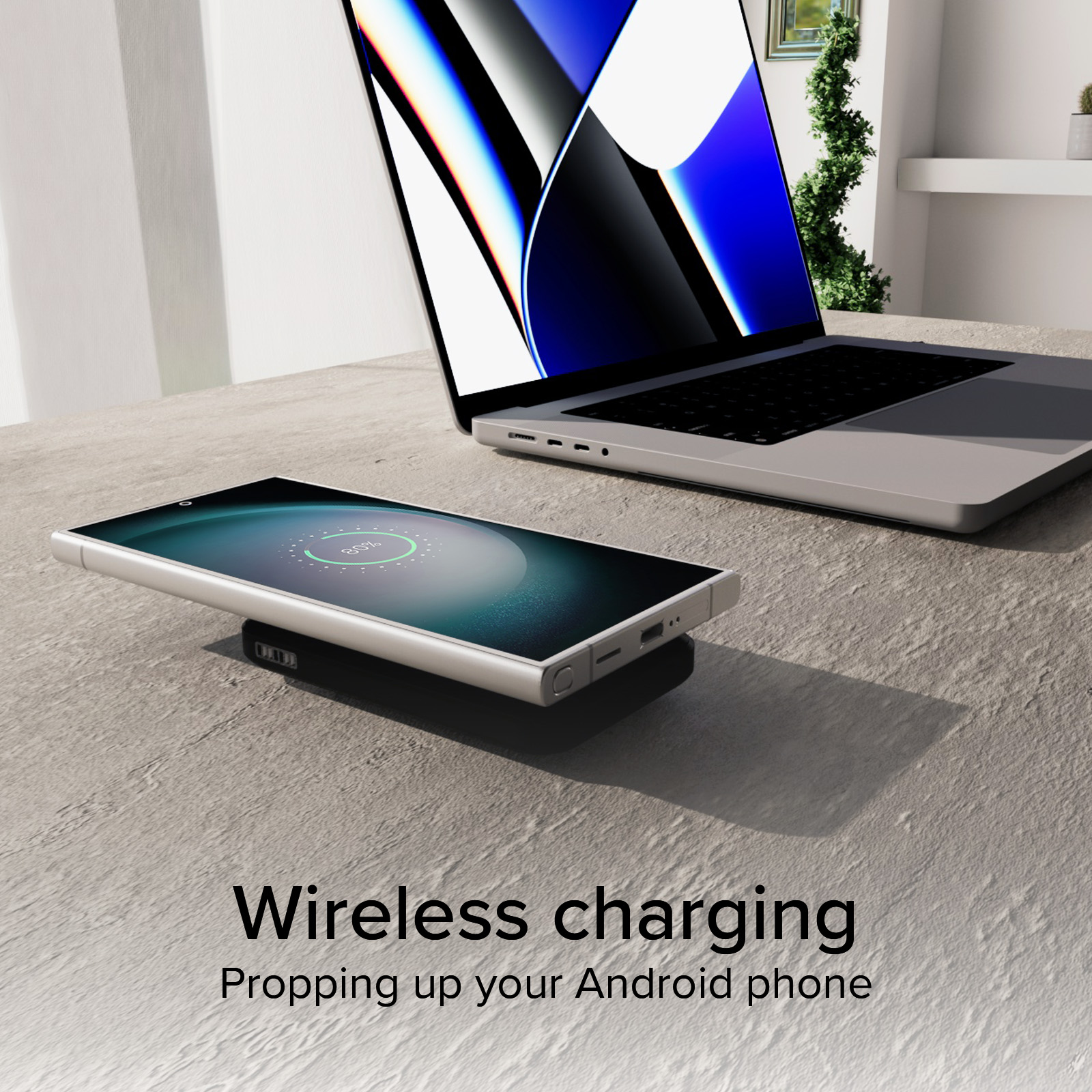 Uno smartphone argentato si ricarica wireless su un pad nero accanto a un laptop aperto.