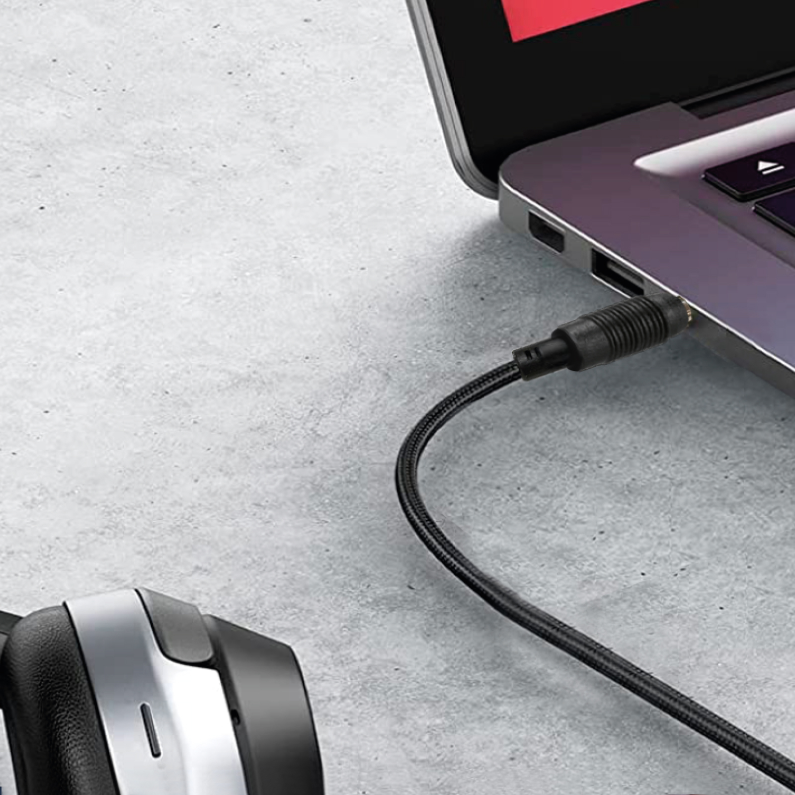 Un cable de audio negro se conecta a un portátil. Auriculares a la izquierda.